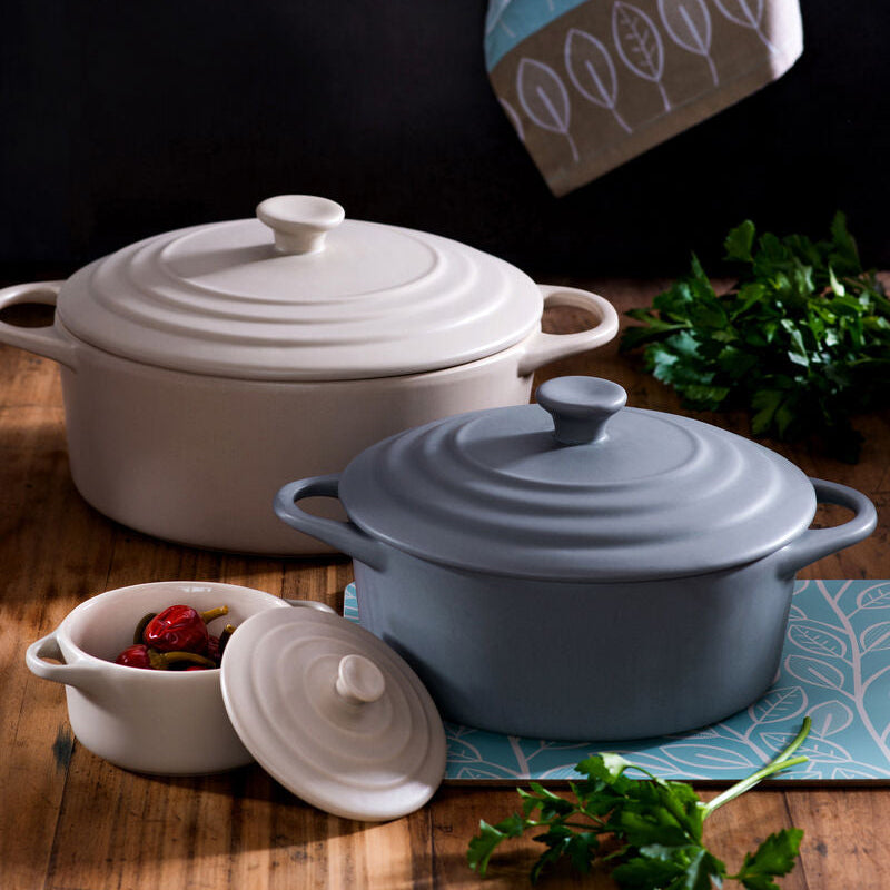 Set of ceramic cookware on a wooden surface with herbs and spices.