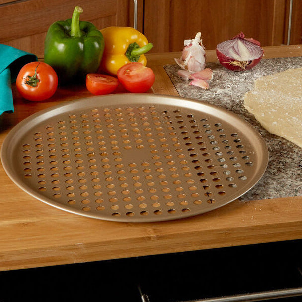 Wooden kitchen counter with pizza dough, vegetables, and a perforated baking tray.