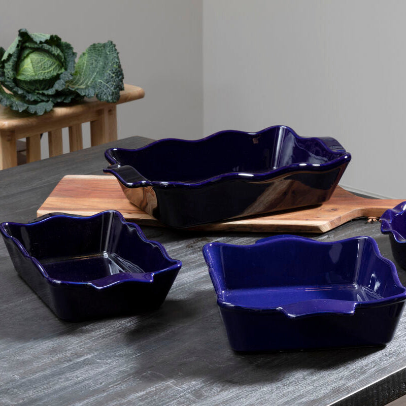 Set of four blue ceramic dishes on a gray surface with green leafy vegetables in the background.
