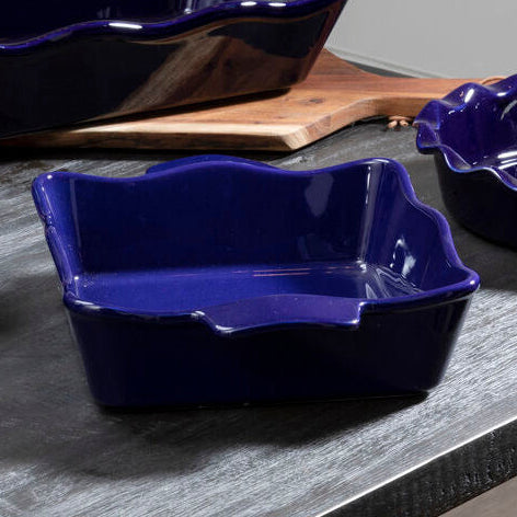 Set of four blue ceramic dishes on a gray surface with green leafy vegetables in the background.