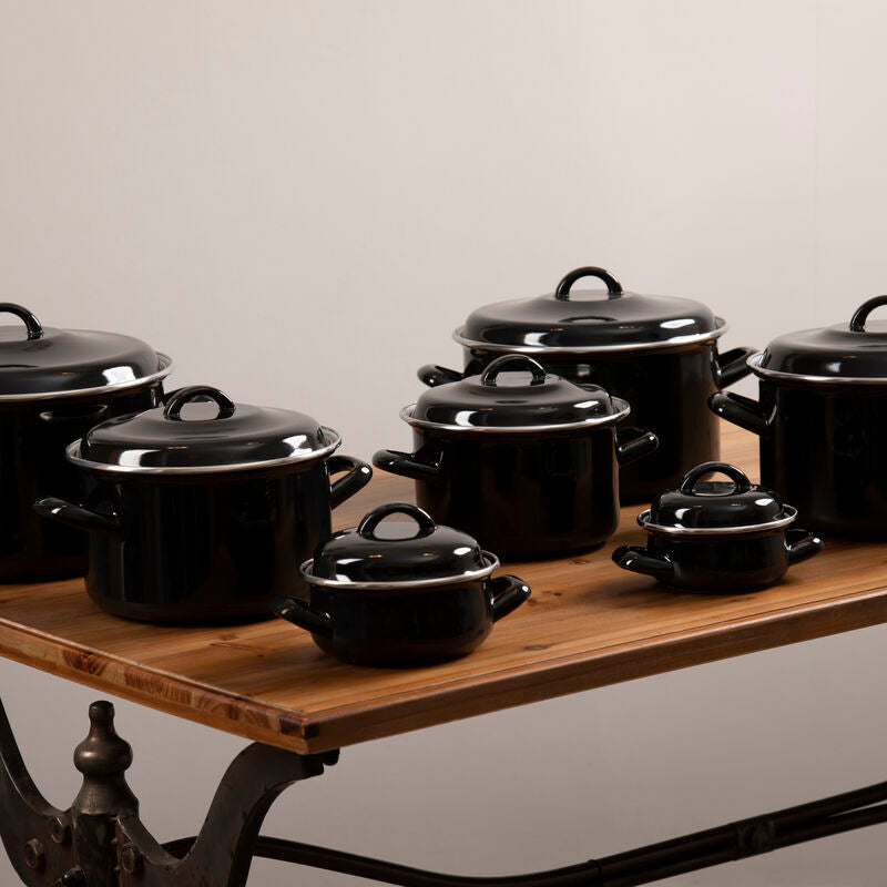 Set of black cookware on a wooden table with a neutral background
