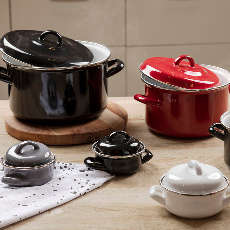 Set of black, red, and white ceramic cookware on a wooden surface.
