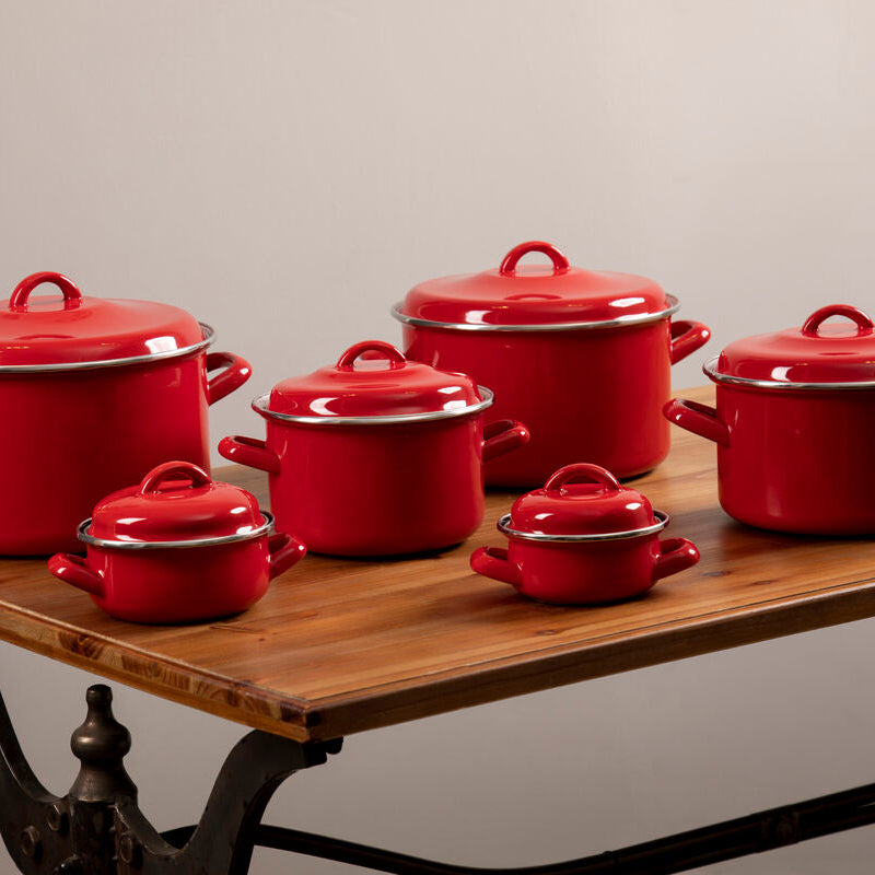 Set of red enameled cookware on a wooden table with a neutral background