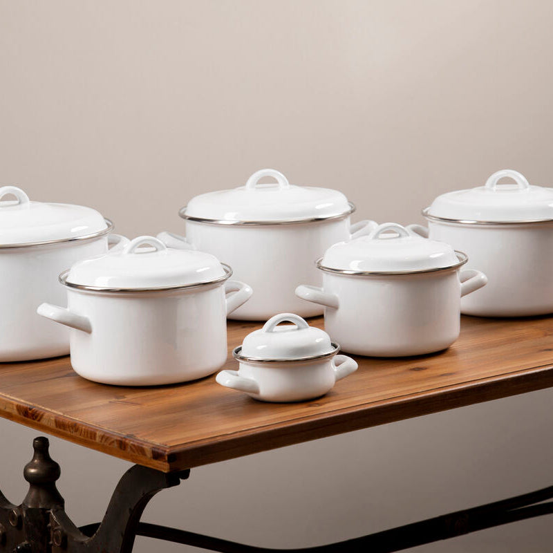 Set of white enameled cookware on a wooden table against a beige background