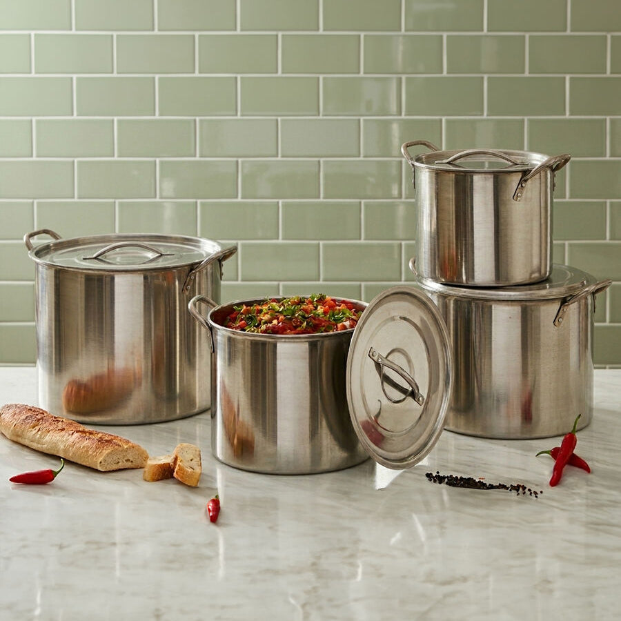 Set of stainless steel pots on a kitchen counter with a tiled wall background