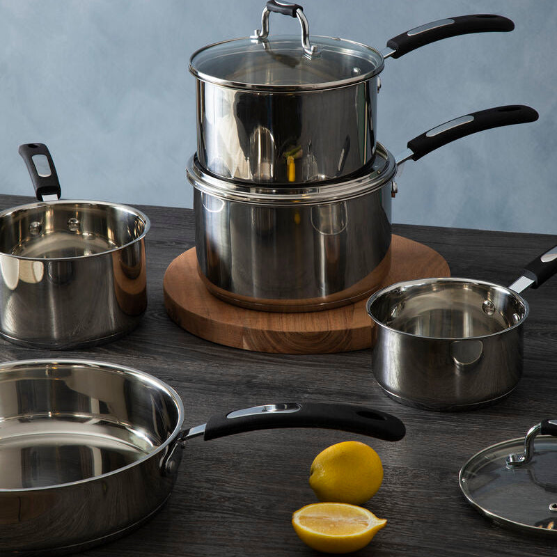 Set of stainless steel cookware on a wooden surface with lemons and asparagus.