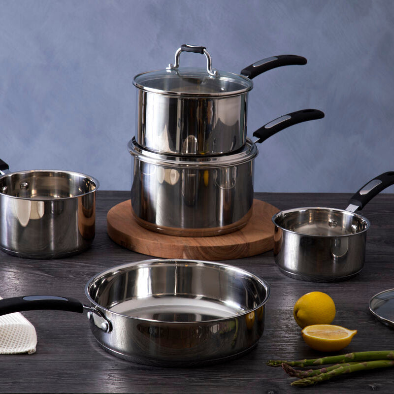 Set of stainless steel cookware on a wooden surface with lemons and asparagus.