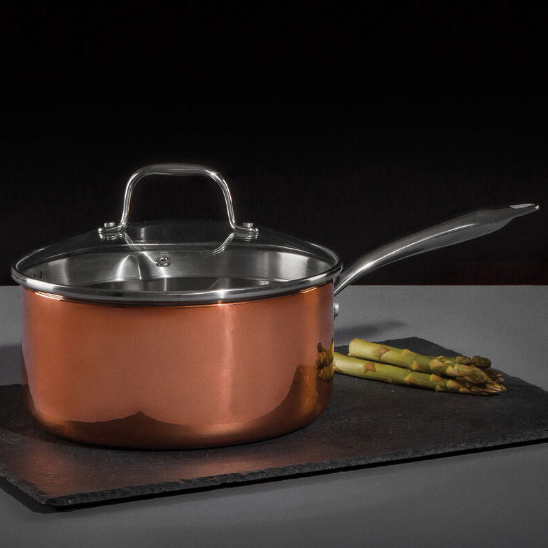 Copper saucepan with lid on a dark surface with asparagus