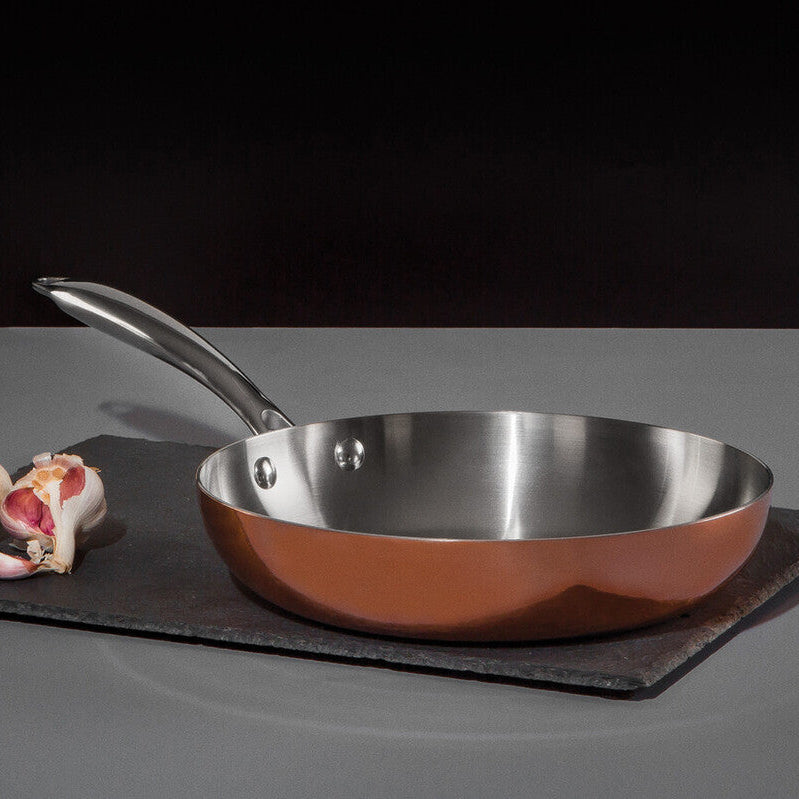 Copper frying pan on a dark surface with garlic and shallots.