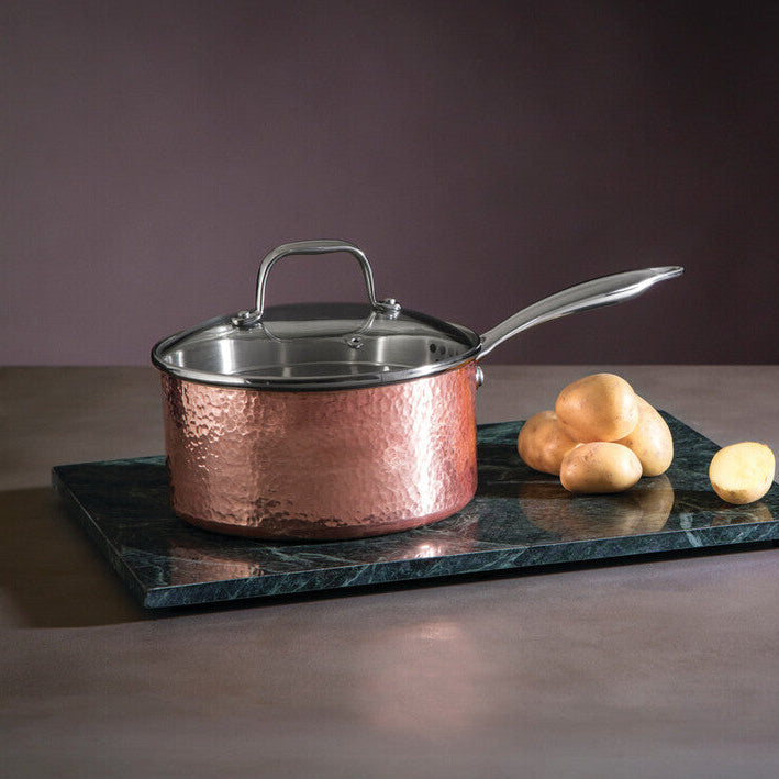 Copper saucepan with lid on a dark marble tray against a dark background
