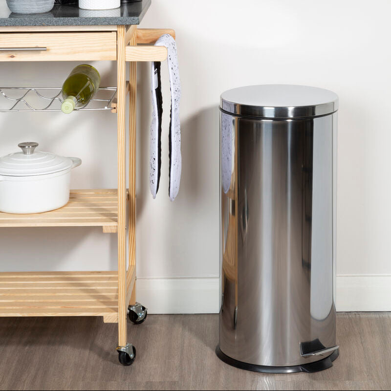 Stainless steel trash can next to a wooden kitchen cart with a white wall background