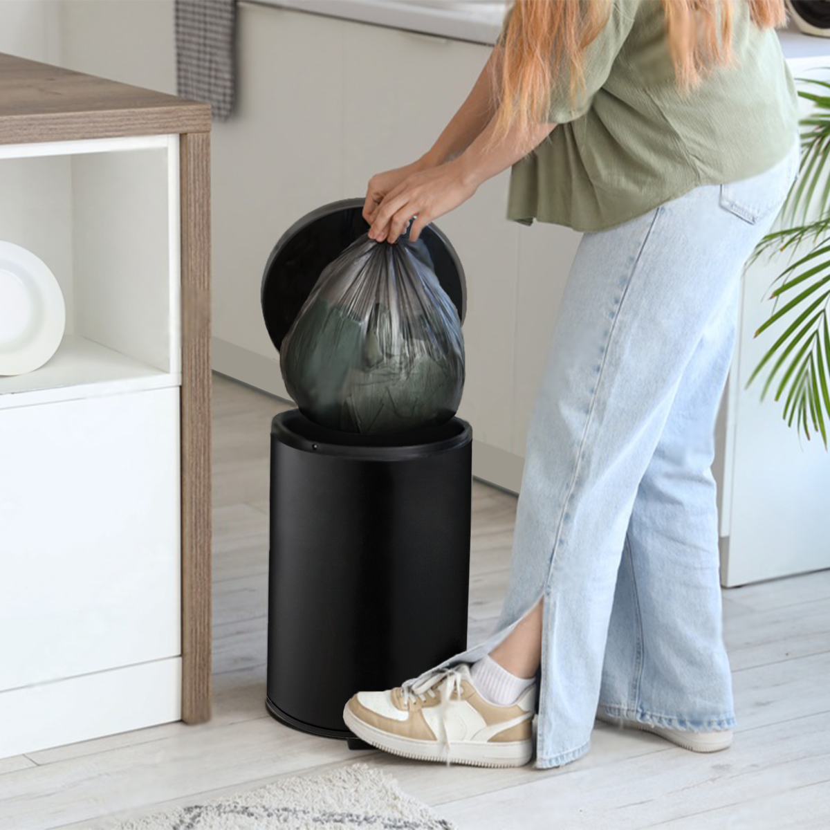 Person putting a trash bag into a black trash can in a room.
