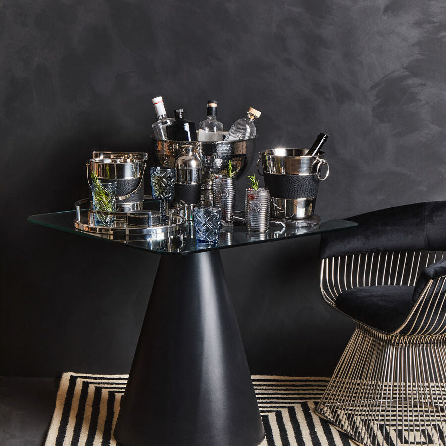 Modern black dining table with glass top and chair against a dark wall.