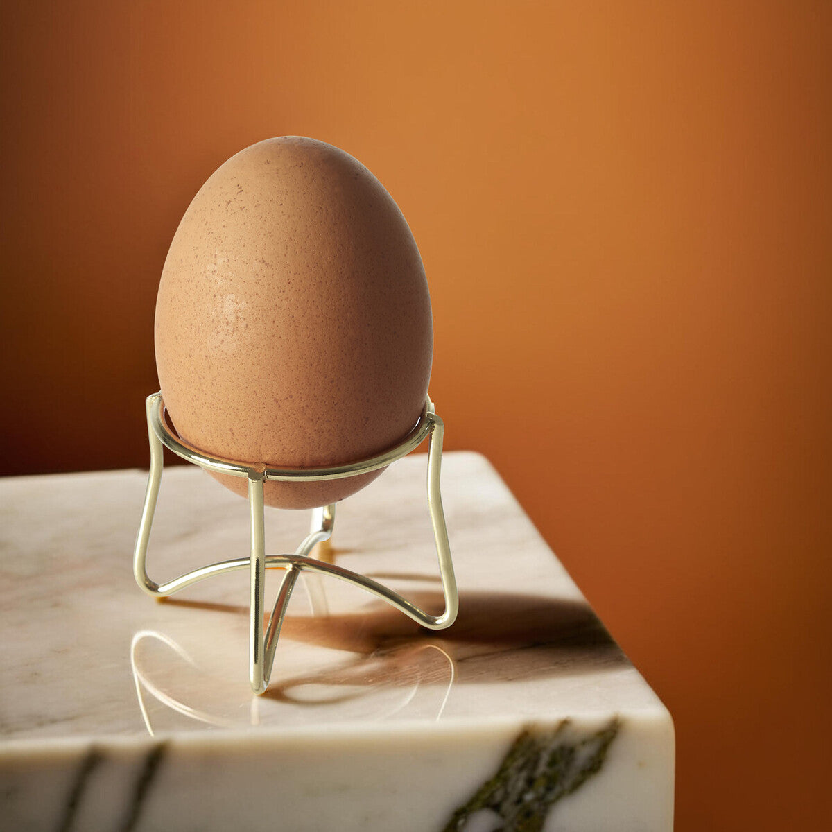 Brown egg on a decorative stand against an orange wall