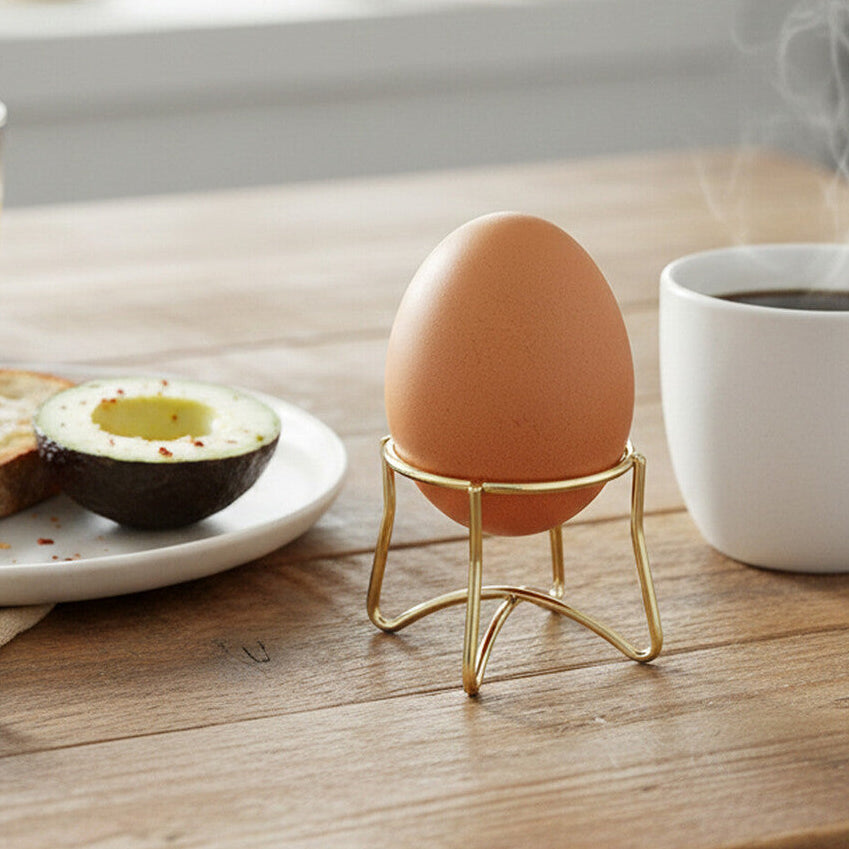 Breakfast scene with toast, avocado, egg in a stand, and coffee on a wooden table.