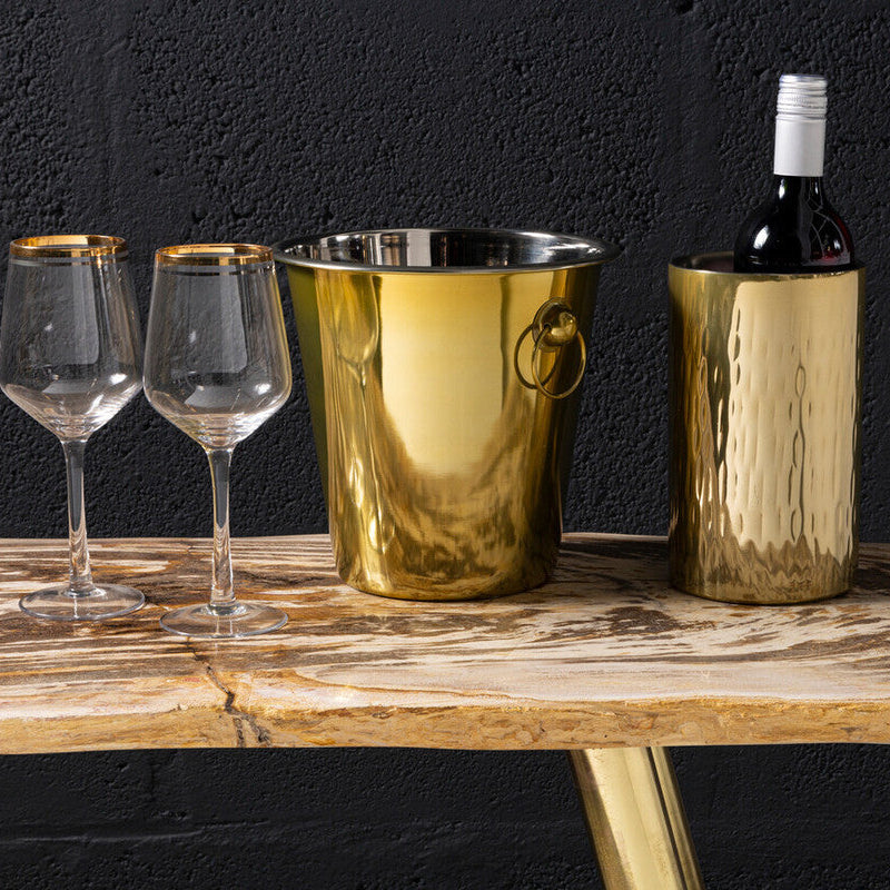 Gold wine bucket and bottle with two glasses on a wooden table against a dark background