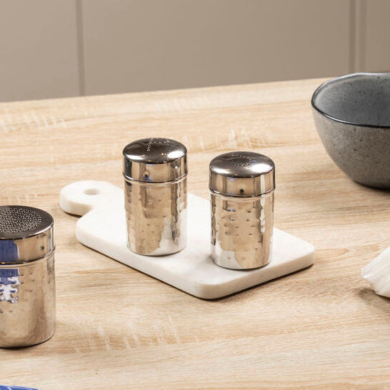 Kitchen setting with gray bowls, silver tumblers, and a cutting board on a wooden table.