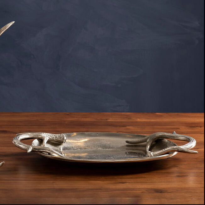 Decorative silver tray with antler design on a wooden surface against a dark background