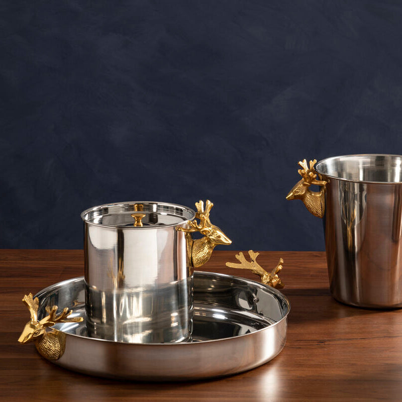 Set of silver drinkware with gold deer handles on a wooden surface against a dark background