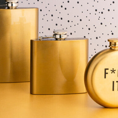 Three gold flasks on a table with a polka dot wall in the background