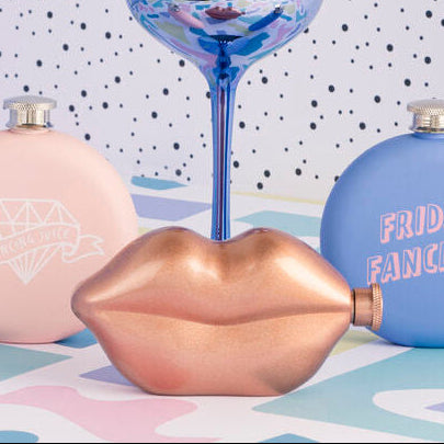Decorative lip-shaped bottles and a wine glass on a patterned surface with a polka dot wall background.