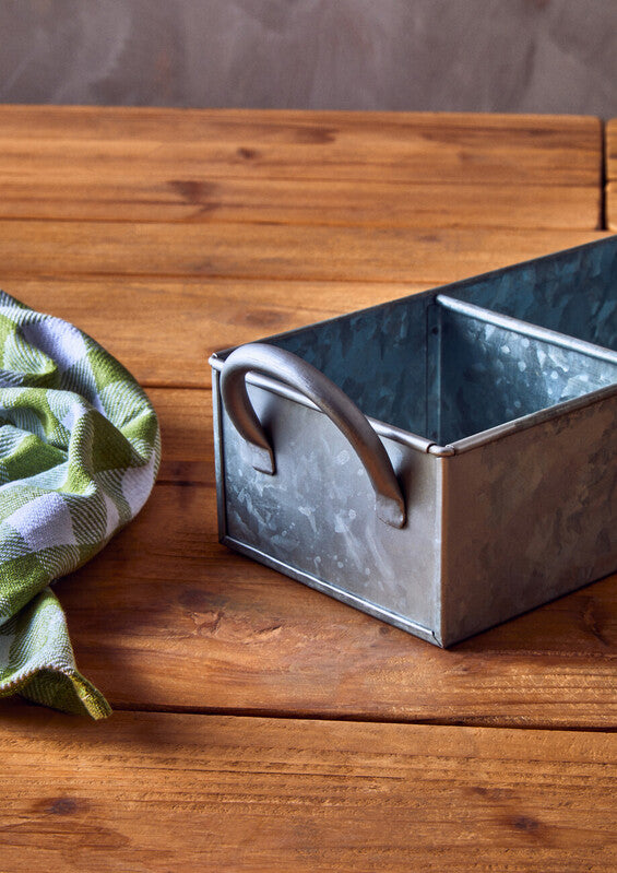 Metal loaf pan on a wooden surface with a green and white checkered cloth.