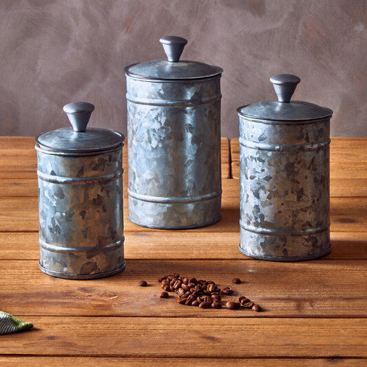 Three metal canisters on a wooden surface with coffee beans in front.