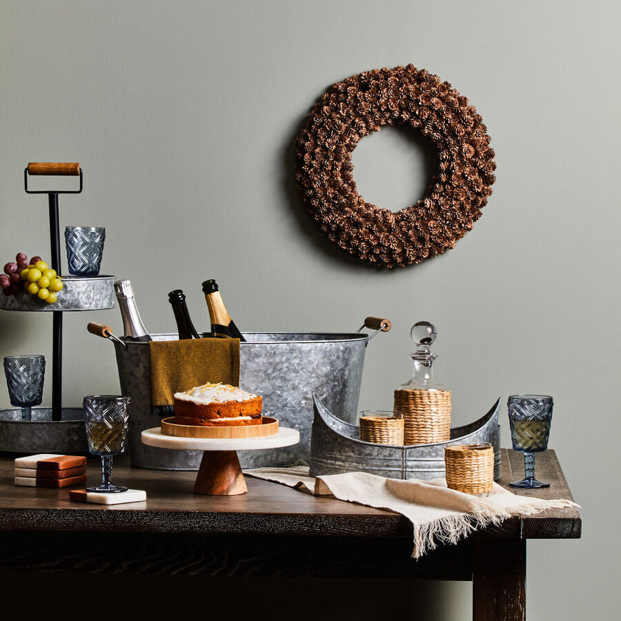 Decorative wreath on a wall with a table featuring a cake, glasses, and other items against a gray background.