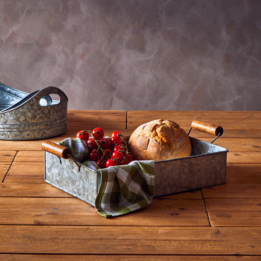 Metal bread basket with loaf of bread and red berries on a wooden table against a gray textured wall.