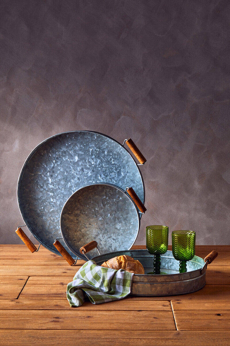 Set of blue ceramic plates with wooden handles on a wooden surface, with green glasses and a towel in the background.