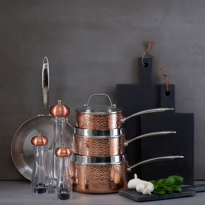 Copper cookware set with kitchen items on a gray surface against a dark background