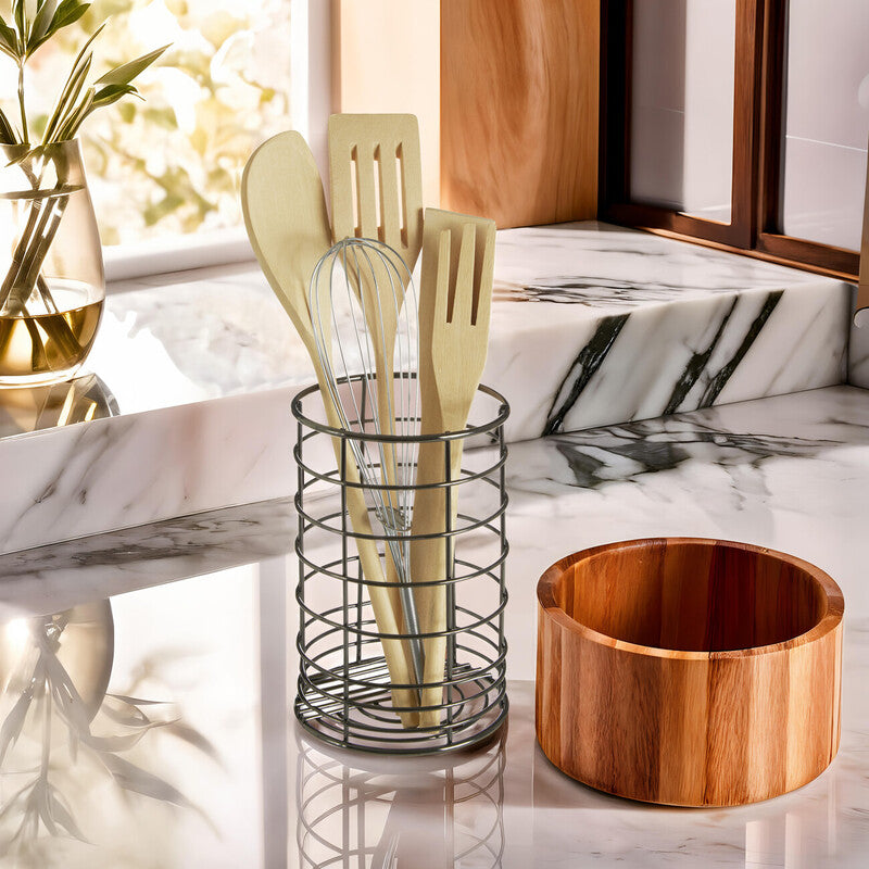 Kitchen utensils in a holder on a marble countertop with a wooden bowl.