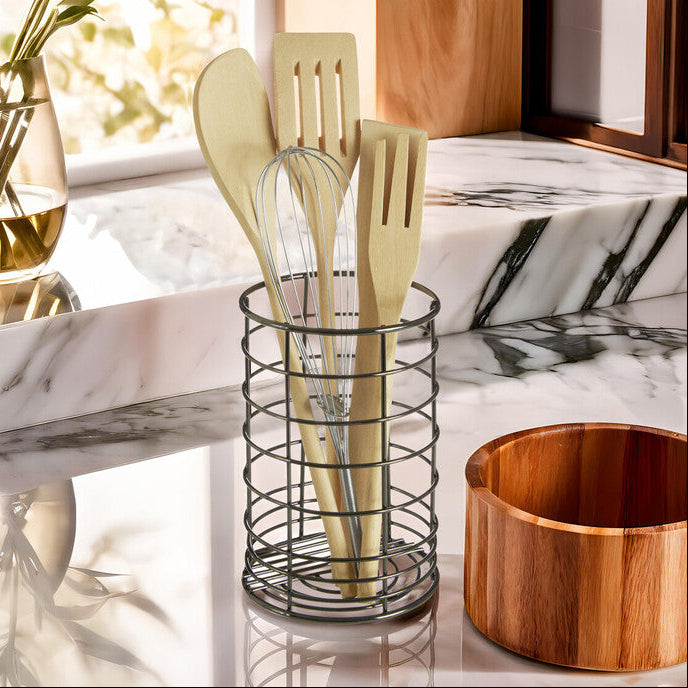 Kitchen utensils in a holder on a marble countertop with a wooden bowl.