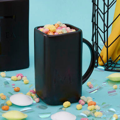 Set of black kitchen utensils including a pitcher, container, and teapot on a blue background with colorful candies.