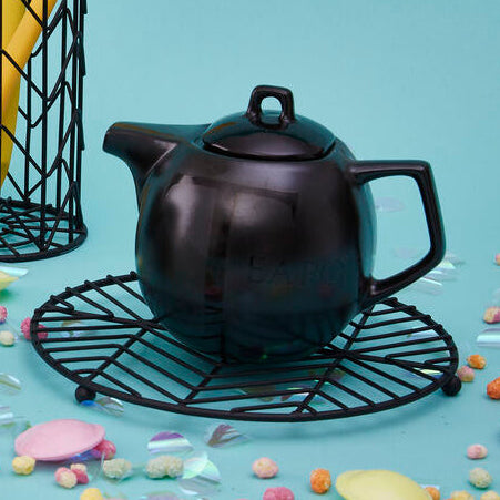 Black teapot and mug with yellow whisk and spoon holder on a blue background with colorful candies.
