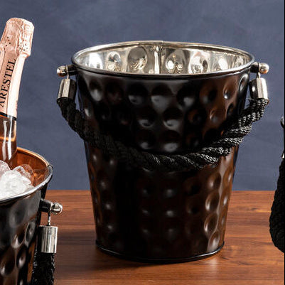 Two bottles of champagne in a black ice bucket on a wooden surface with a dark blue background.