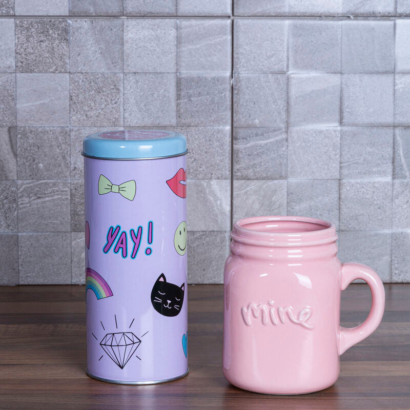 Pink mug and purple cylindrical container with various designs on a wooden surface with tiled wall background