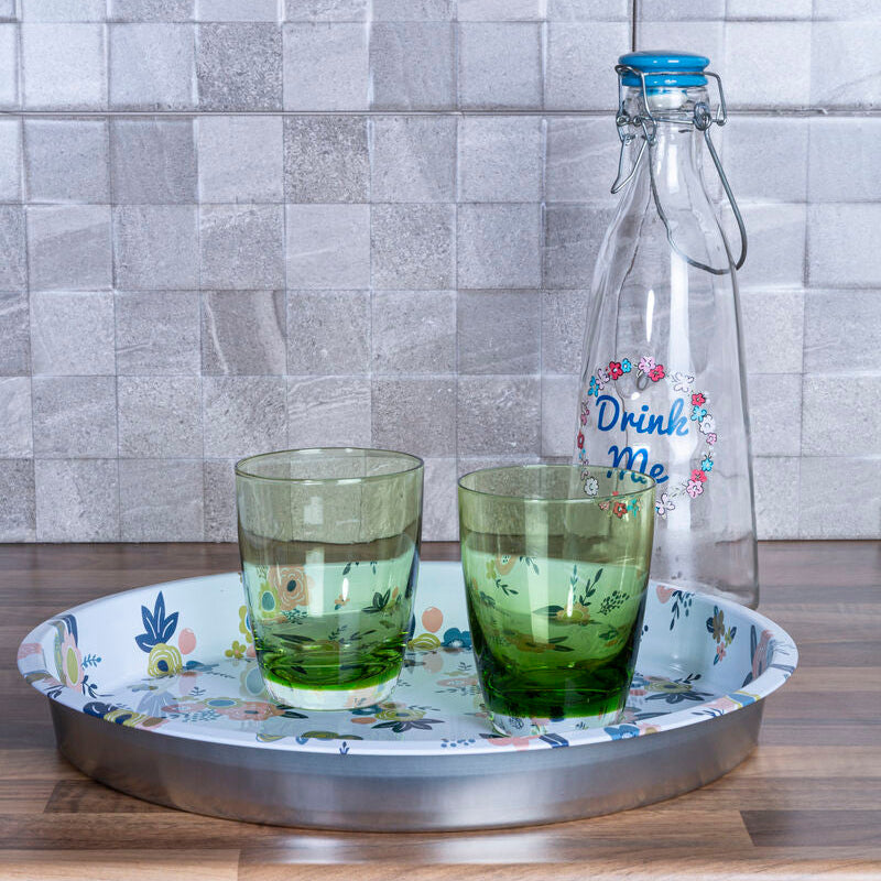 Two glasses with green liquid on a decorative tray with a bottle in the background against a tiled wall.