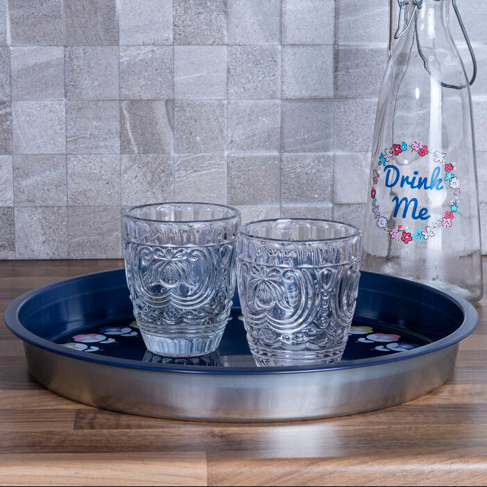 Two glasses on a tray with a decorative bottle against a tiled wall.