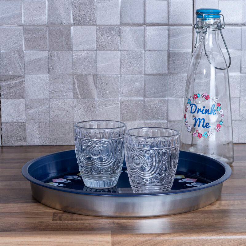 Two glasses on a tray with a decorative bottle against a tiled wall.