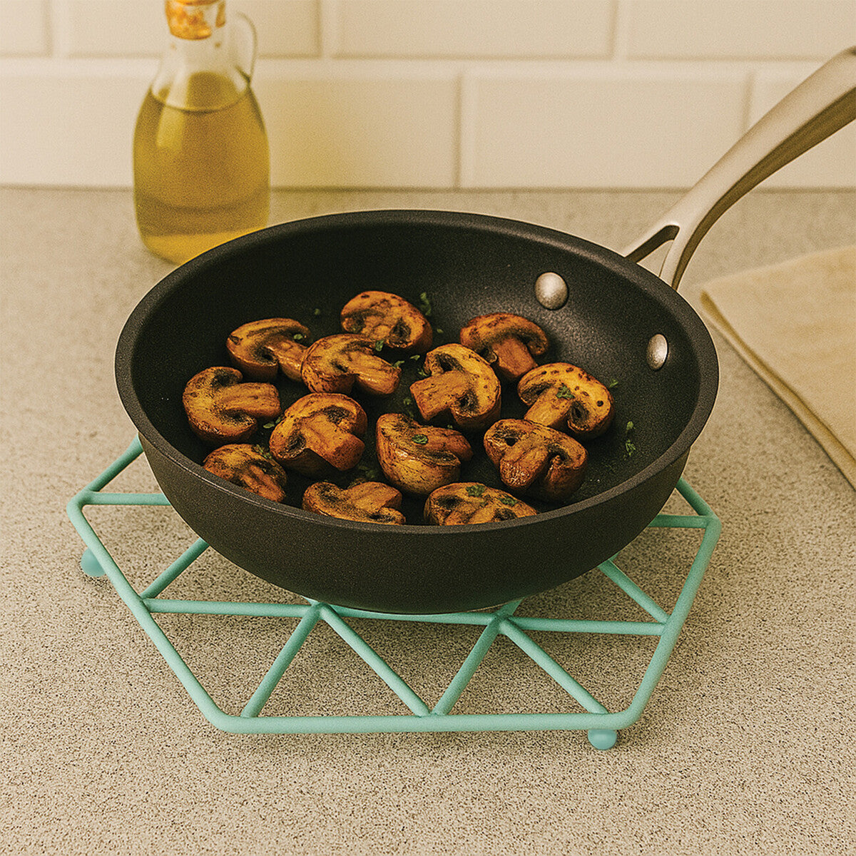 Frying pan with mushrooms on a teal trivet on a countertop.