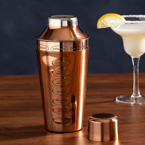 Copper cocktail shaker with a glass of creamy cocktail on a wooden surface
