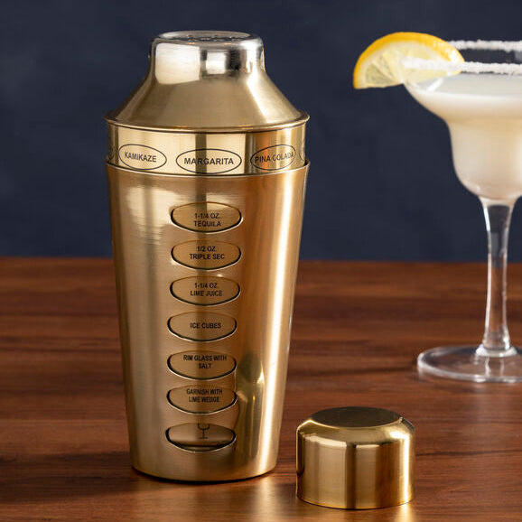 Gold cocktail shaker with a glass of margarita on a wooden surface
