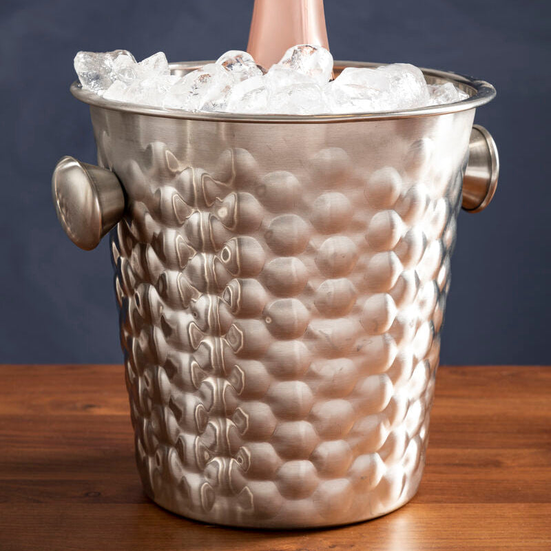 Bottle of champagne in a textured silver ice bucket on a wooden surface with a dark background