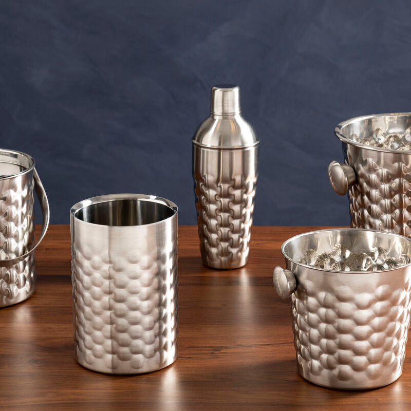Set of silver cocktail shakers and ice buckets on a wooden surface with a dark blue background