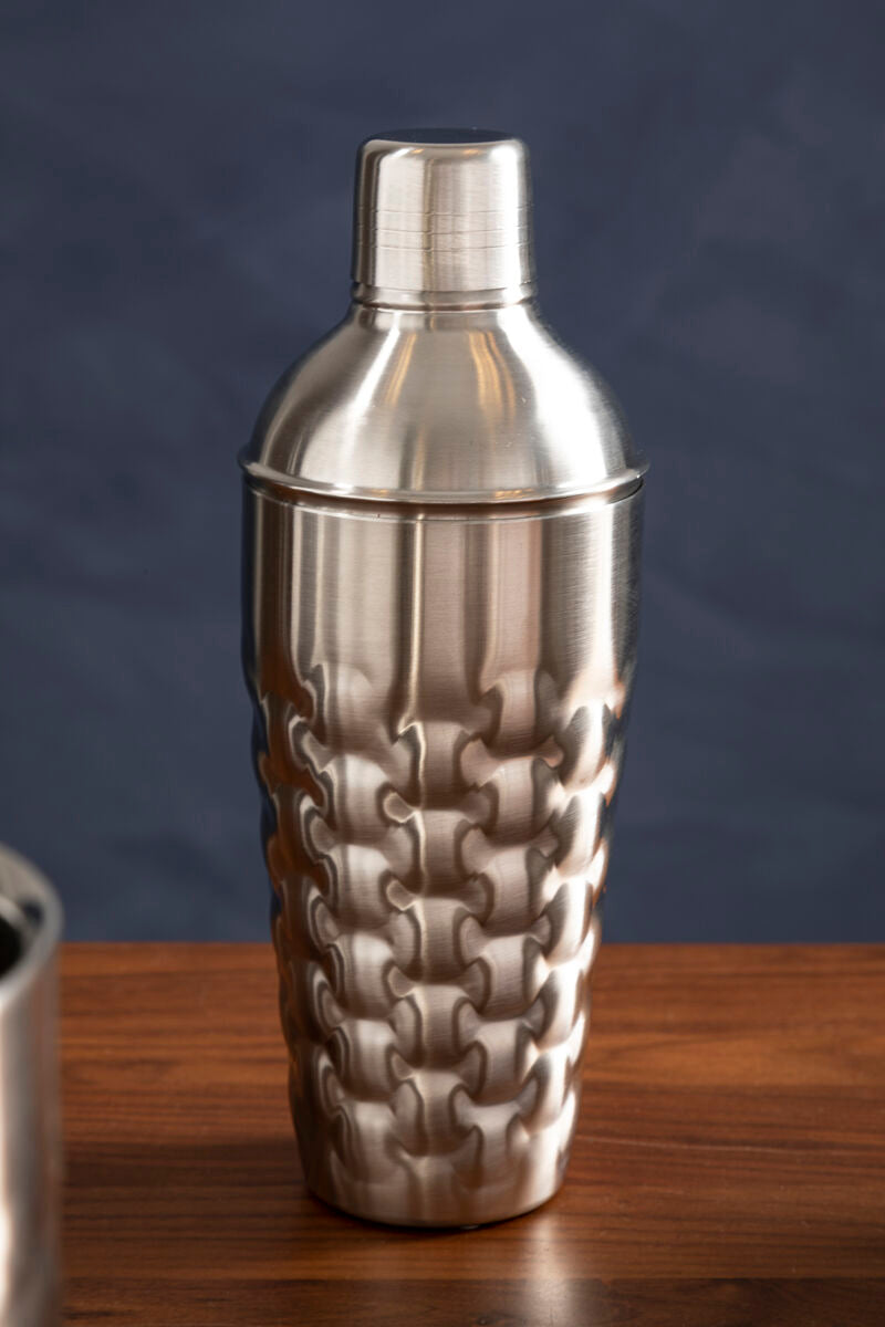 Silver textured cocktail shaker on a wooden surface with a dark blue background