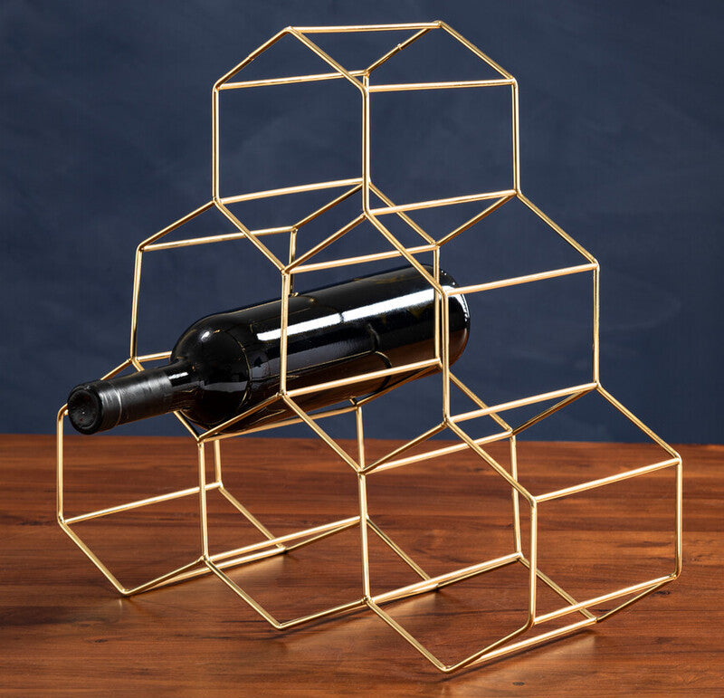 Gold geometric wine bottle holder with a wine bottle on a wooden surface and dark blue background