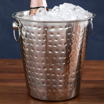 Bottle of pink champagne in a silver ice bucket on a wooden surface with a dark background