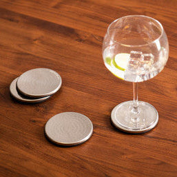 Clear glass with lime wedge on a coaster next to two other coasters on a wooden surface