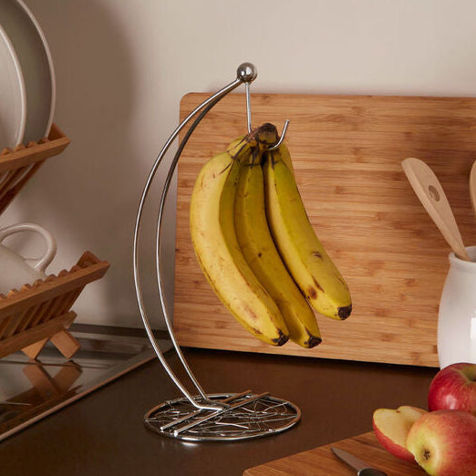 Banana holder with bananas on a kitchen counter with apples and utensils.
